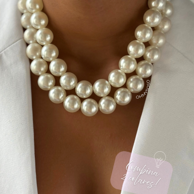 Colar de pérolas grandes e brancas no pescoço com blazer branco e texto Promocional