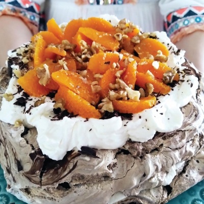 Bolo pavlova com chantilly, noz e tangerina em prato azul, segurado por pessoa com blusa bordada