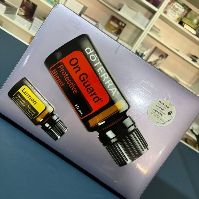 Caixa metálica lilás com óleo essencial doTERRA On Guard e Lemon sobre mesa azul