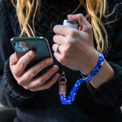 Pulseira azul com padrão branco presa a peça metálica cilíndrica na mão segurando smartphone