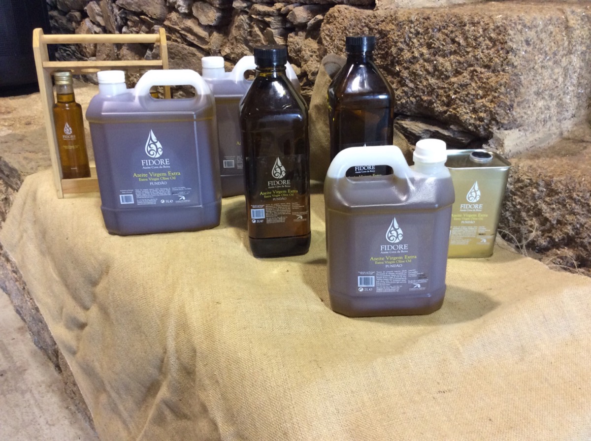 Embalagens de azeite em garrafas de plástico e vidro castanho sobre tecido bege com fundo de pedra