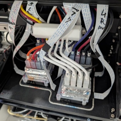 Interior de equipamento eletrônico com cabos multicoloridos e fitas flexíveis brancas com inscrições.