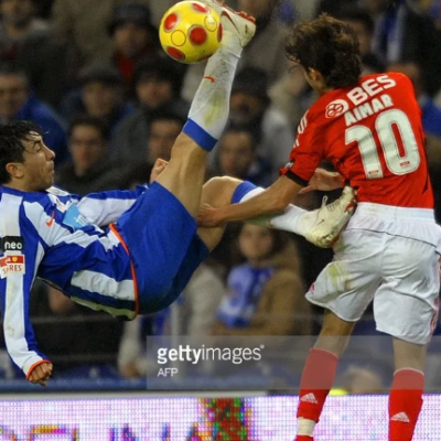 Dois jogadores de futebol em ação, um a fazer remate de bicicleta com bola amarela com manchas vermelhas.