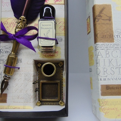Conjunto de escrita com tinteiro, suporte metálico e caneta com fita roxa dentro de caixa decorada