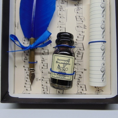 Conjunto de pena azul, tinteiro com etiqueta, rolo de papel com pauta musical sobre fundo com pauta musical