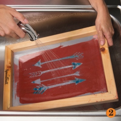 Quadro de serigrafia com stencil de setas azuis a ser lavado na pia.