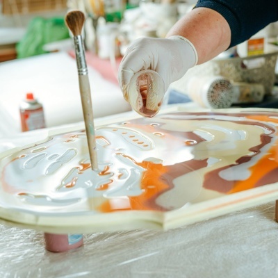 Mão com luva a despejar tinta numa superfície plana com várias cores de tinta líquida e pincel em pé
