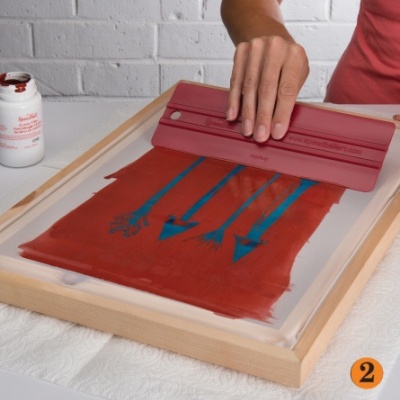 Ecrã de serigrafia com tinta vermelha e setas azuis, usada por uma pessoa com camisola vermelha