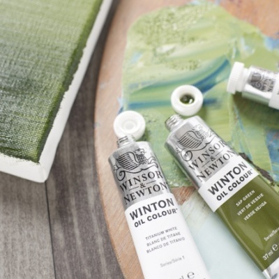 Tubos de tinta a óleo Winsor & Newton, cores Titanium White e Sap Green, sobre paleta com tinta e tela com pintura verde