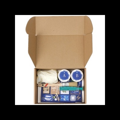 Caixa aberta com dois recipientes A e B, luvas, pincel, espátula e pacote azul com imagens brancas.