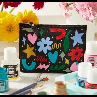 Carteira preta com padrão colorido de flores e estrelas sobre mesa com tintas e pincéis