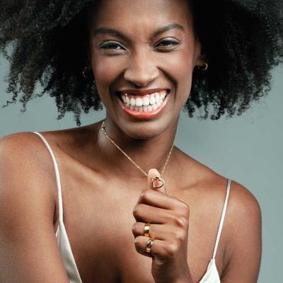 Mulher sorridente com colar e anéis dourados e top branco