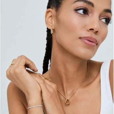 Mulher com colar, brincos, anéis e pulseiras douradas e prateada, vestindo top branco