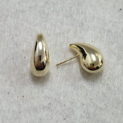 Brincos dourados de formato irregular sobre fundo cinza claro