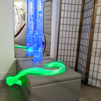 Suporte cinzento liso com tubos luminosos azuis e fibras óticas verdes junto a biombo branco