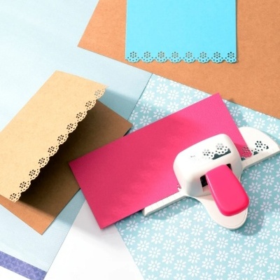 Folhas de papel coloridas com bordas recortadas em padrão floral e um furador de papel branco e rosa