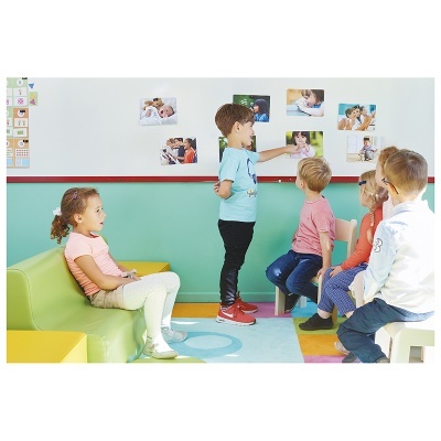 Crianças em sala colorida com móveis infantis e fotografias na parede.