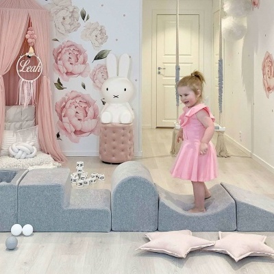 Quarto infantil com decoração em tons rosa e cinzento e menina vestida de rosa