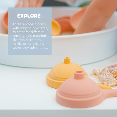 Dois funis de silicone amarelo e rosa sobre superfície branca com conchas decorativas próximo a tigela e mãos de criança