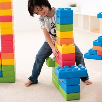 Criança a brincar com blocos de construção coloridos grandes num quarto claro