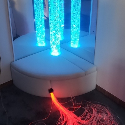 Coluna de bolhas azul com fibras óticas vermelhas no chão junto a um espelho