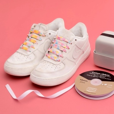 Sapatilhas brancas com cadarços florais e fita de cetim rosa sobre fundo rosa