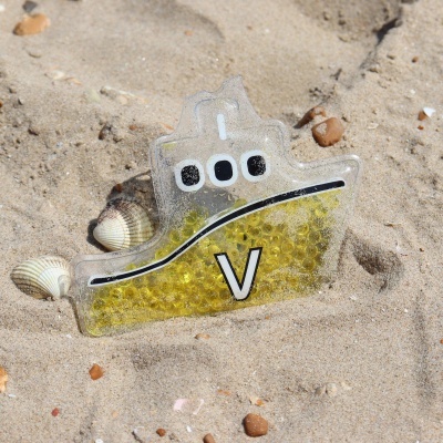 Brinquedo em forma de barco transparente com bolinhas amarelas na areia