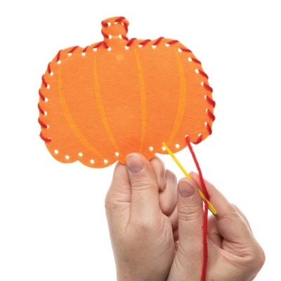 Peça em feltro laranja em forma de abóbora com costura vermelha e amarela, segurada por mãos.