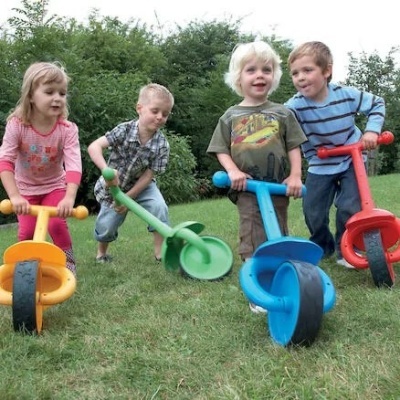 Crianças a brincar em trotinetes coloridas de plástico no relvado