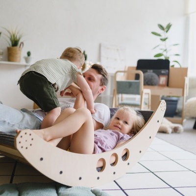 Crianças e adulto brincando com baloiço de madeira em sala acolhedora