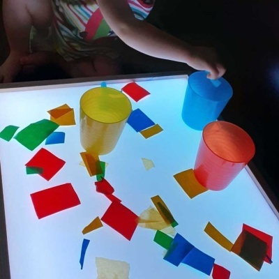 Copos de plástico coloridos sobre superfície iluminada com pedaços de papel colorido e braço de criança