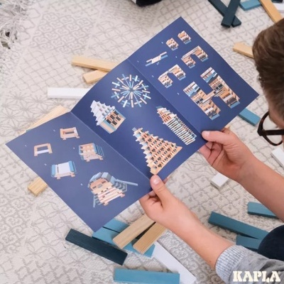 Manual de construções em madeira KAPLA com tábuas azuis e naturais no chão.