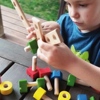 Criança a brincar com jogo de montagem em madeira colorida numa mesa exterior