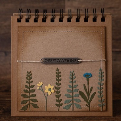 Caderno castanho com flores desenhadas e etiqueta metálica OBSERVATIONS