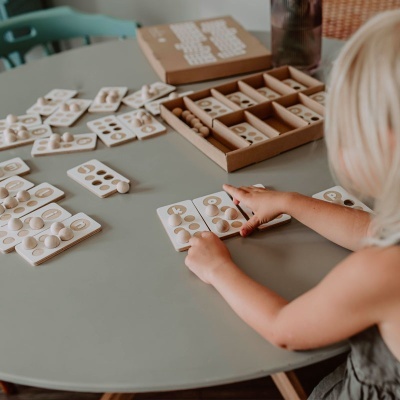 Criança a jogar com brinquedo educativo de madeira numa mesa redonda cinza.