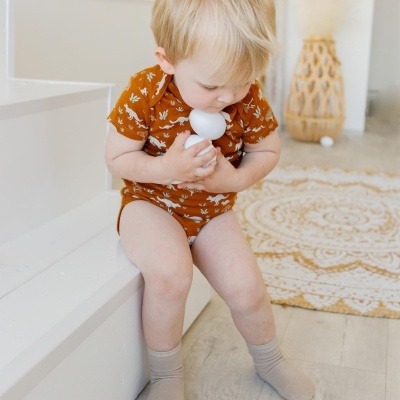 Criança com body ferrugem e padrão branco segurando brinquedo branco sentada na escada