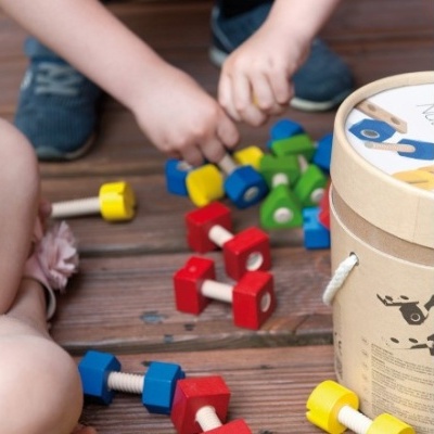 Brinquedos de madeira coloridos para montar, com recipiente cilíndrico e pavimento de madeira.