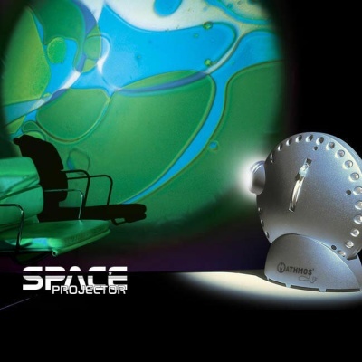 Projetor de luz metálico prateado com projeção verde e azul abstrata e cadeiras verdes ao fundo