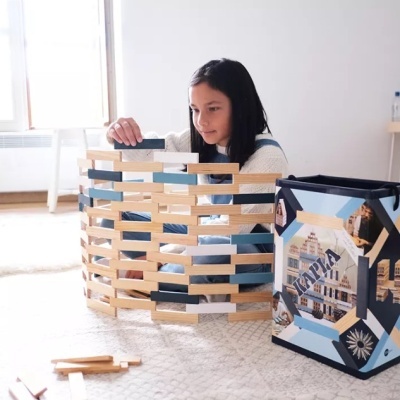 Menina a construir estrutura com peças de madeira colorida junto a caixa azul decorada