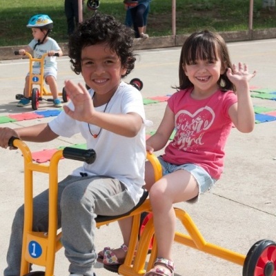 Crianças a andar em triciclo amarelo com detalhes em vermelho e azul