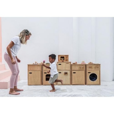 Mobiliário infantil de madeira estilo cozinha com detalhes pintados em ambiente claro com mulher e criança.