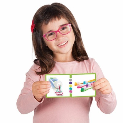 Criança de óculos e camisola rosa segura cartão com imagens de pasta e escovas de dentes coloridas