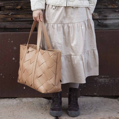 Mala bege de couro sintético entrelaçada nas mãos de uma pessoa com saia clara e botas pretas