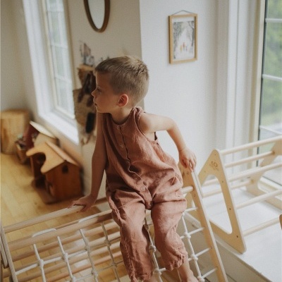 Menino sentado numa rede de corda branca numa estrutura de madeira clara