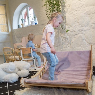 Crianças em ambiente interior com paredes brancas, brincando com móveis de madeira e almofada roxa