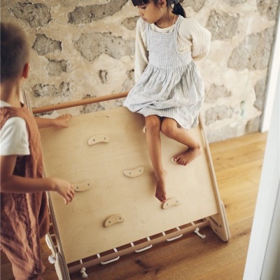 Crianças a brincar em estrutura de escada de madeira com apoios para mãos em ambiente interior com parede de pedra e chão de madeira