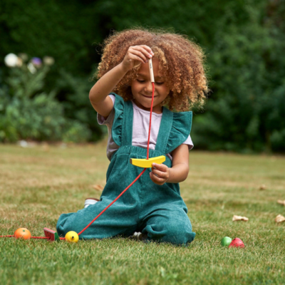 Criança a brincar com brinquedo de madeira colorido ao ar livre na relva
