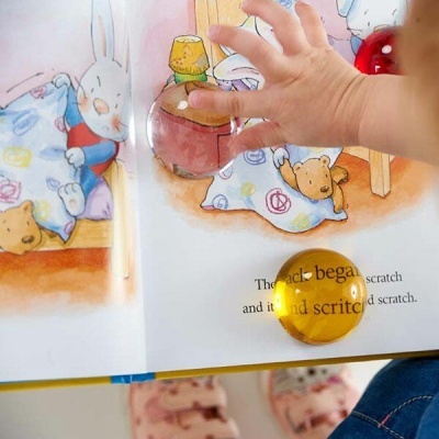 Livro infantil aberto com ilustrações e uma pedra amarela transparente sobre a página