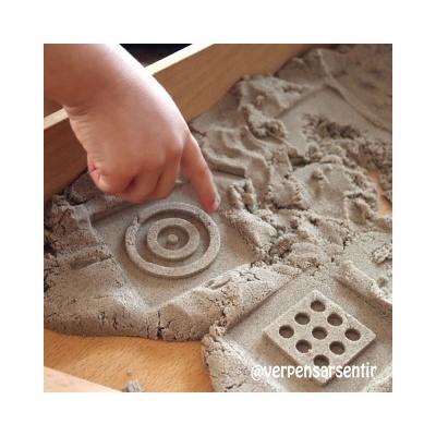 Caixa de areia moldável com padrões e mão de criança a tocar