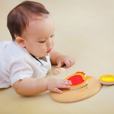 Bebé a brincar com brinquedo educativo de madeira com peças vermelha, amarela e natural no chão claro